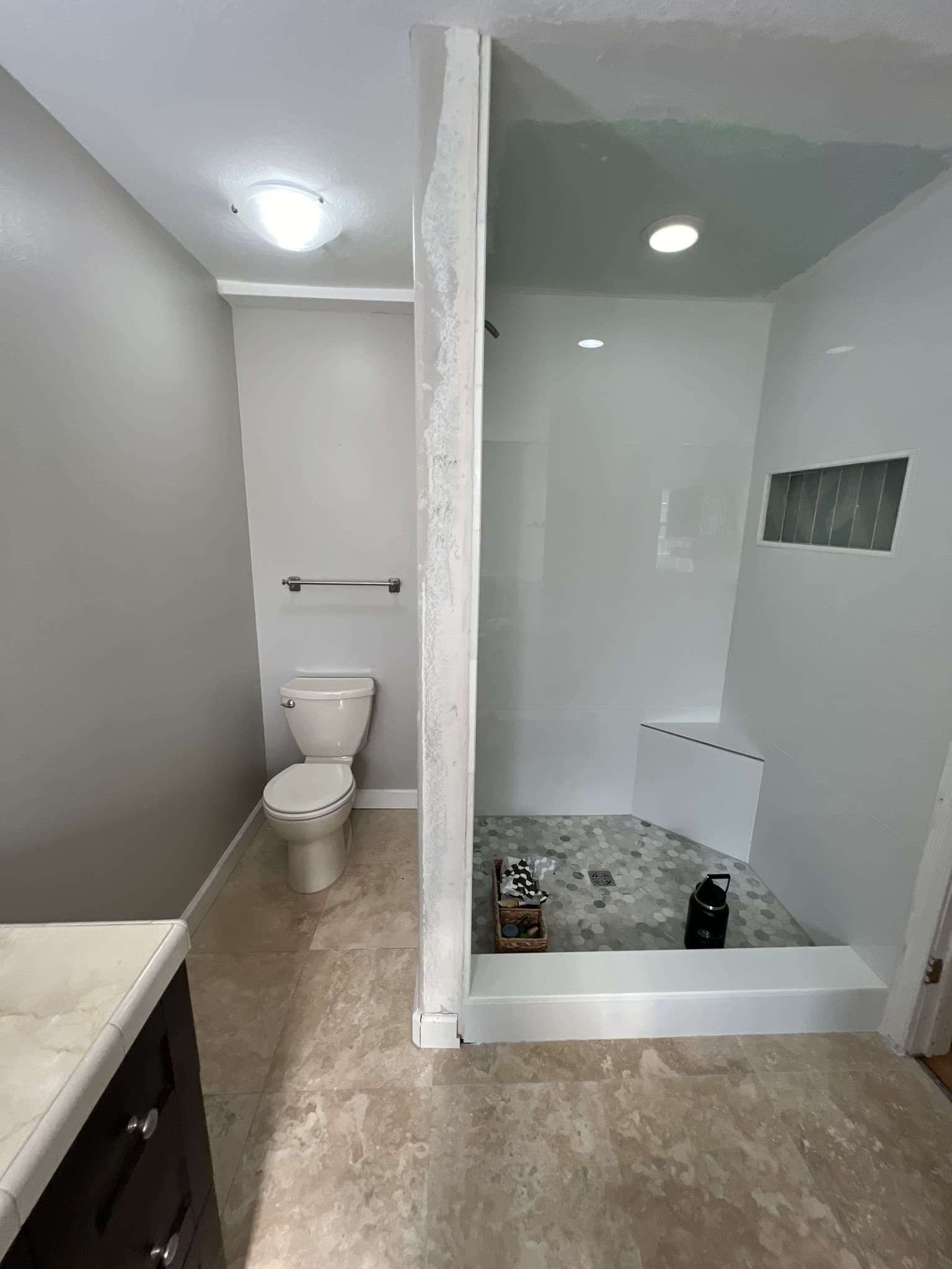 Walk-in doorless shower with white tile walls, built-in bench and blue-gray hexagon mosaic floor — Karhan Construction, Orlando