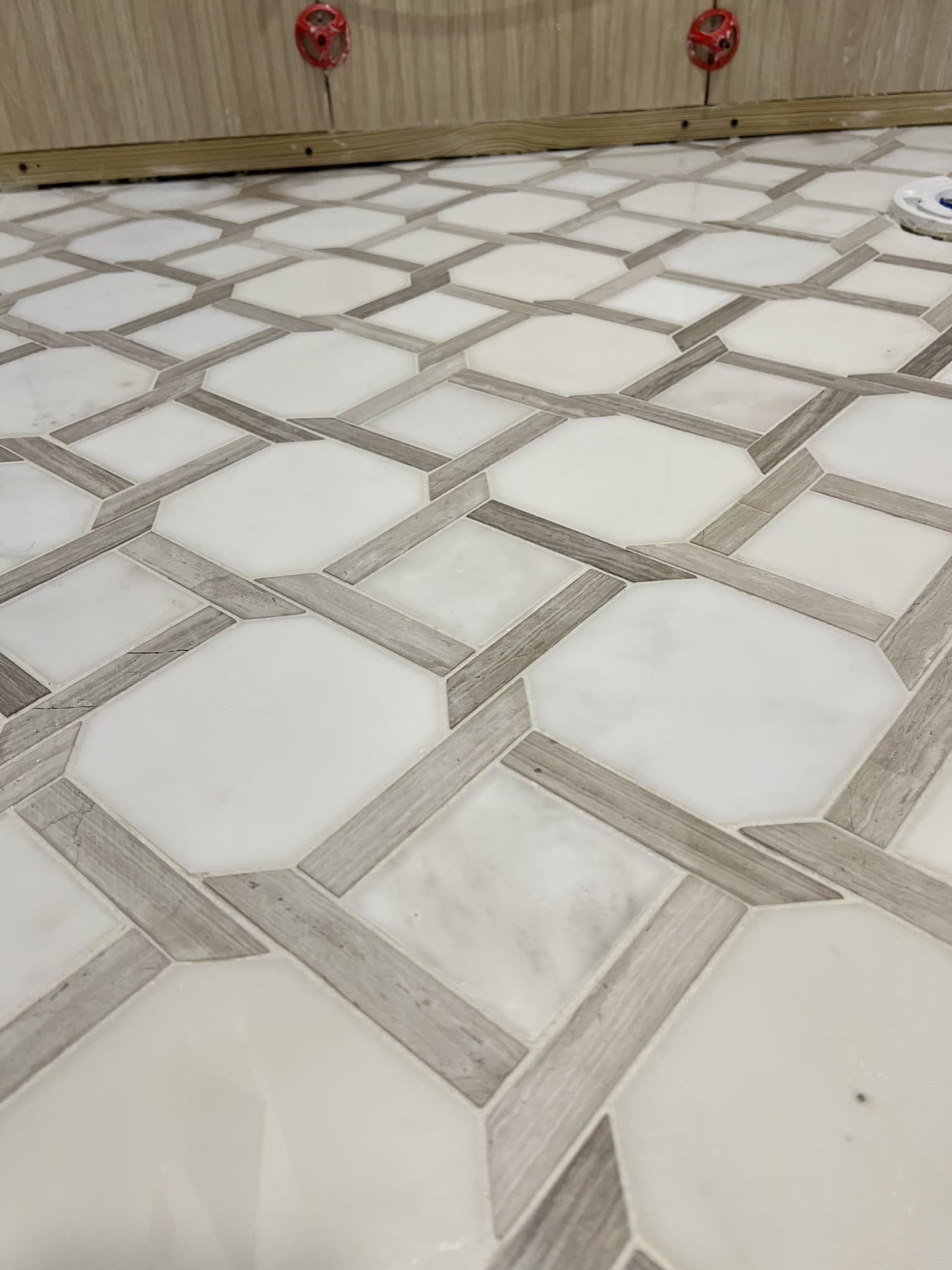 Marble octagon floor tile with gray wood-look strips forming a lattice pattern around a toilet flange — Karhan Construction, Orlando