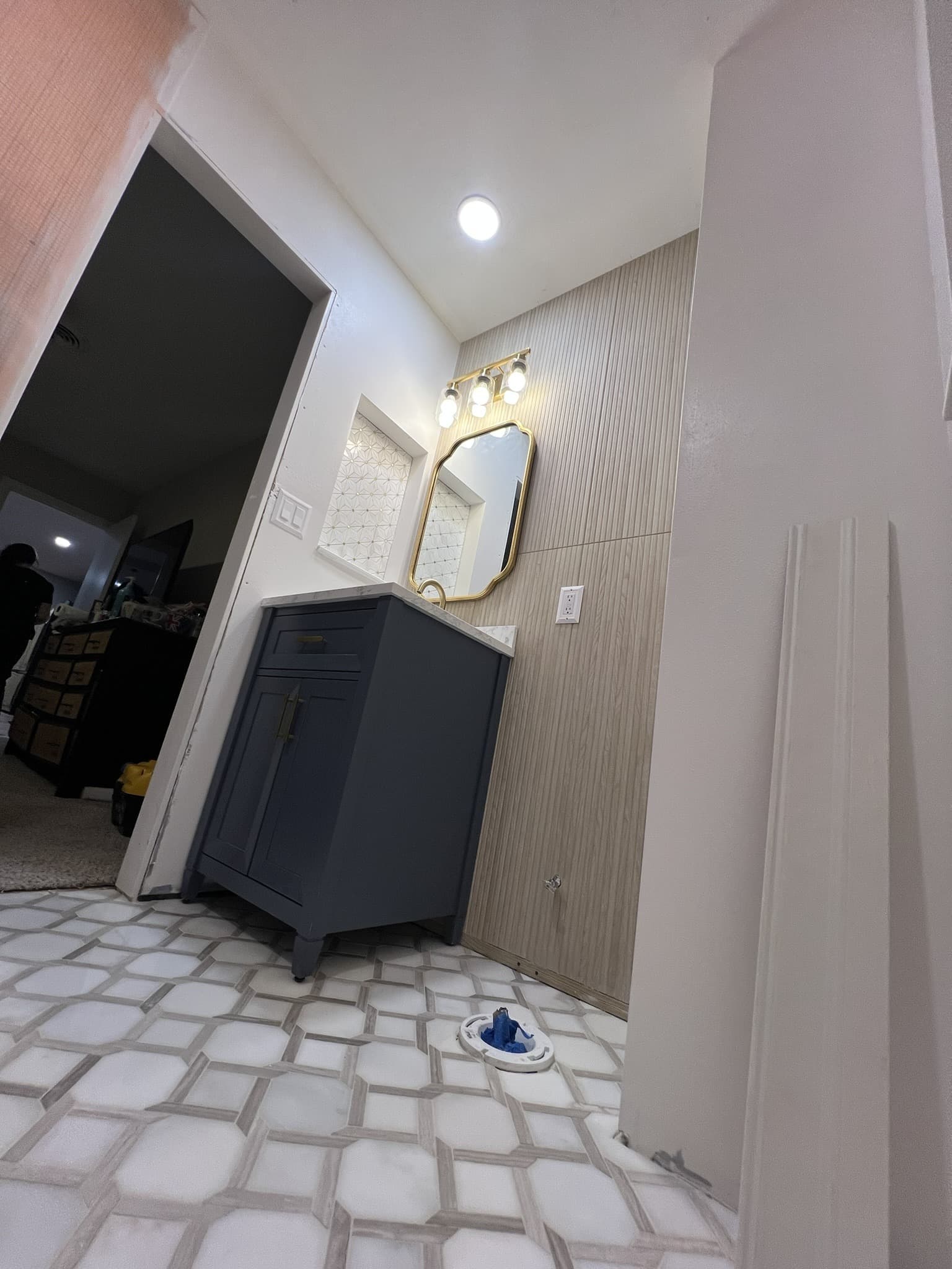 Navy vanity and gold mirror under a 3-bulb gold light with white-and-gray geometric marble floor tile — Karhan Construction, Orlando