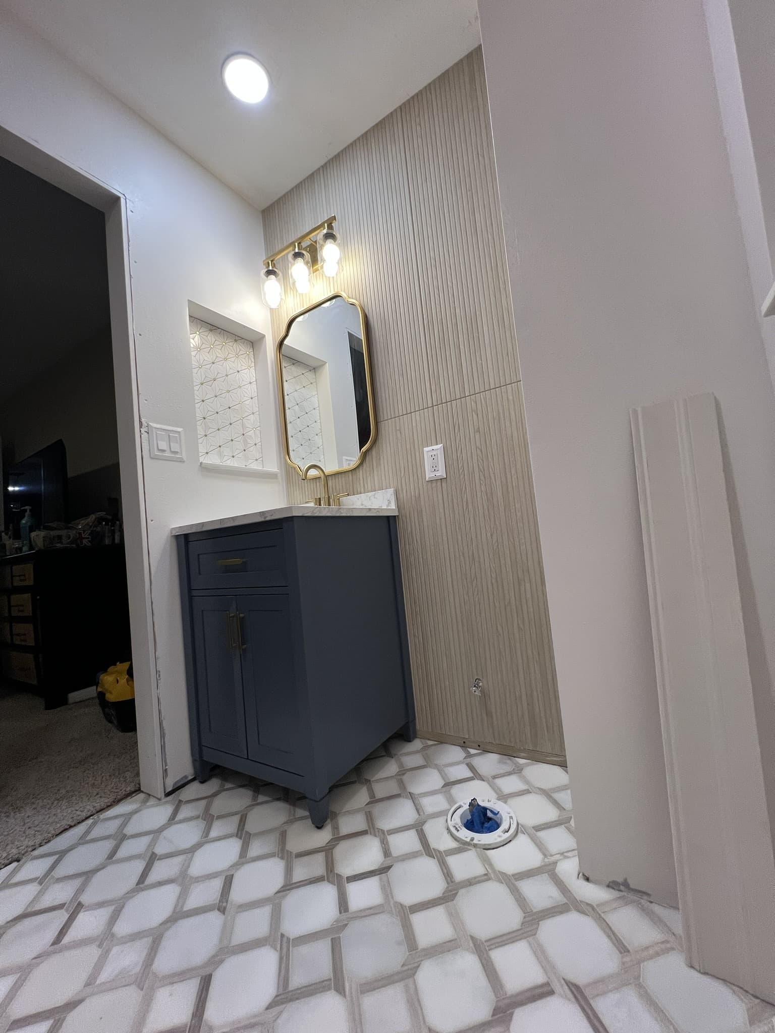 Blue vanity with marble top and gold vanity light, wood-plank accent wall and diamond-pattern marble floor — Karhan Construction, Orlando