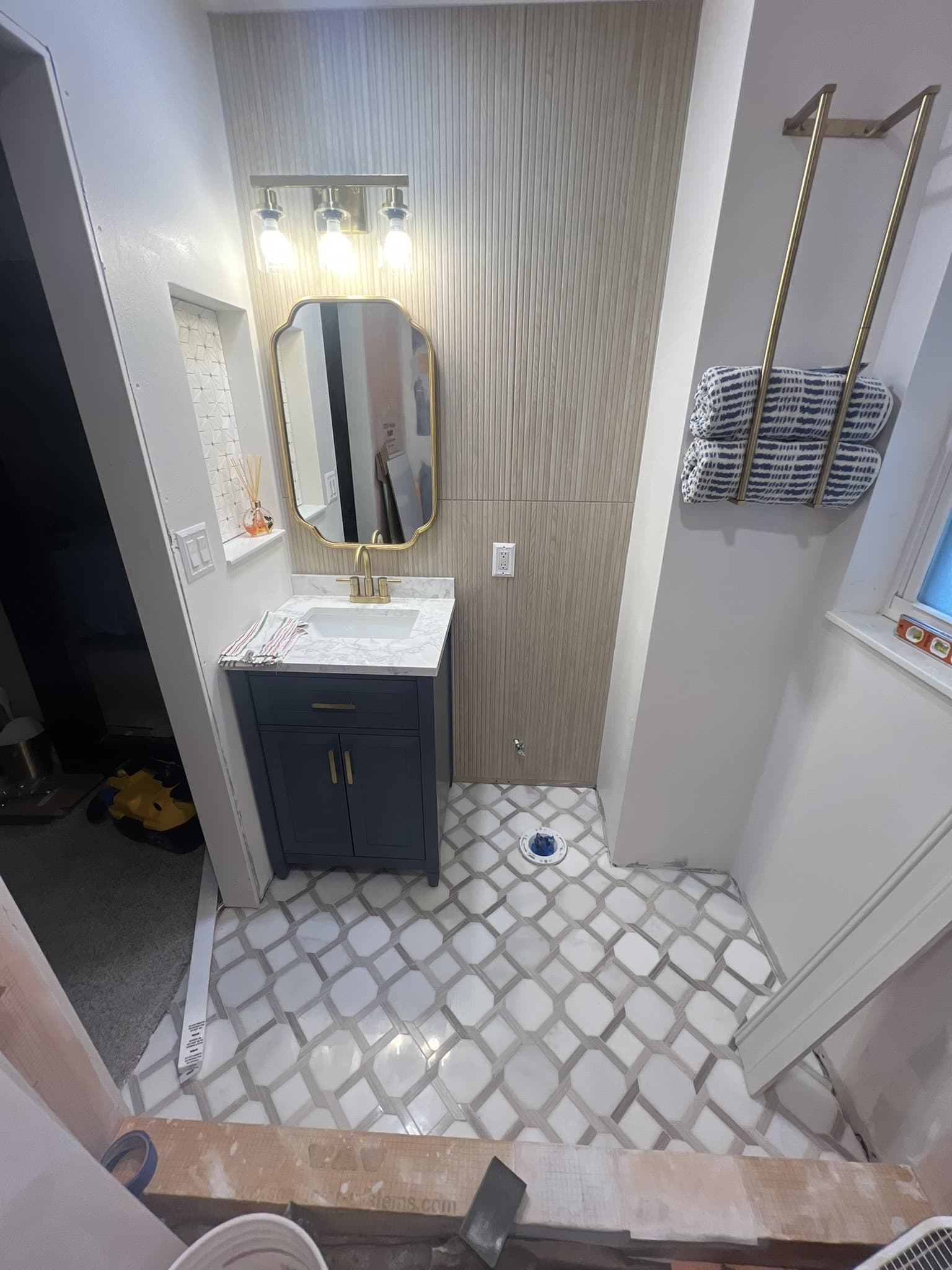 Small bathroom with navy vanity, gold fixtures, lattice marble floor and navy towels on gold bars — Karhan Construction, Orlando