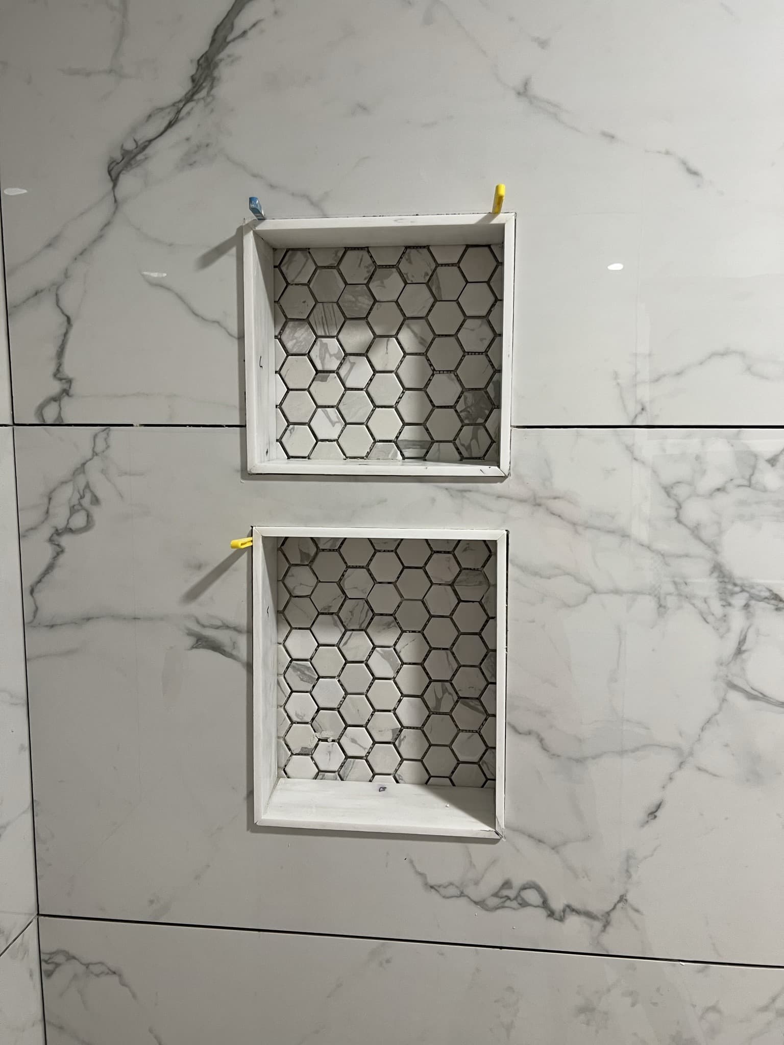 Two stacked square shower niches with white marble hexagon mosaic backs set in veined marble-look tile — Karhan Construction, Orlando