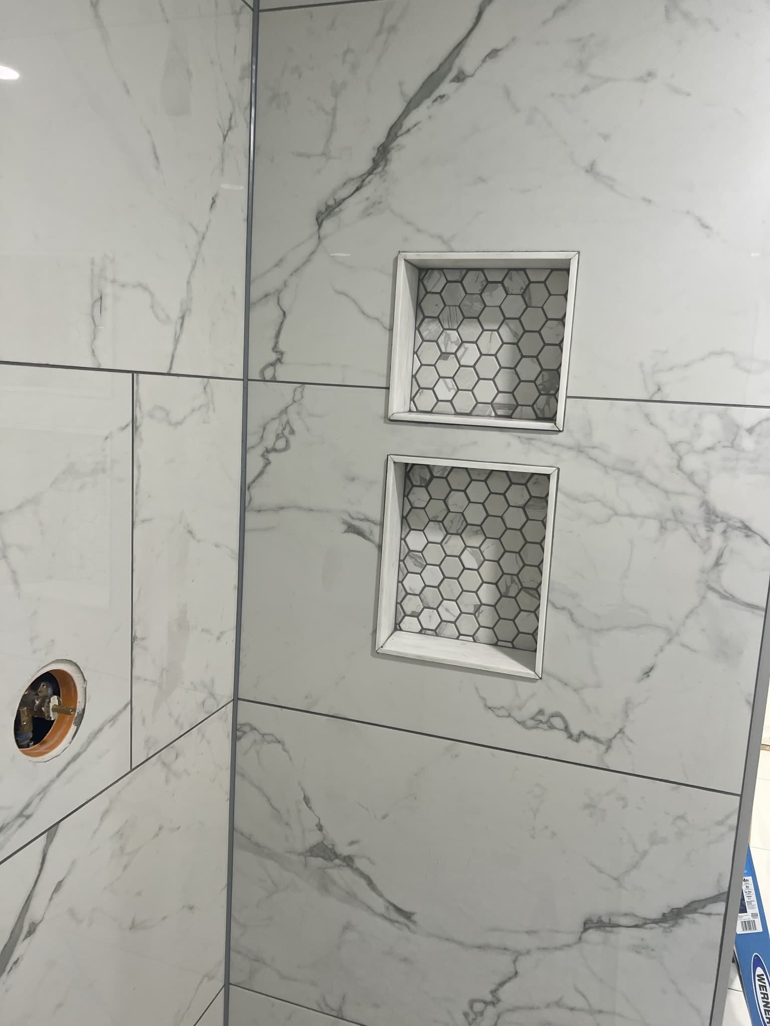 Angled marble-look shower wall with two recessed hexagon-mosaic niches and a shower valve opening — Karhan Construction, Orlando