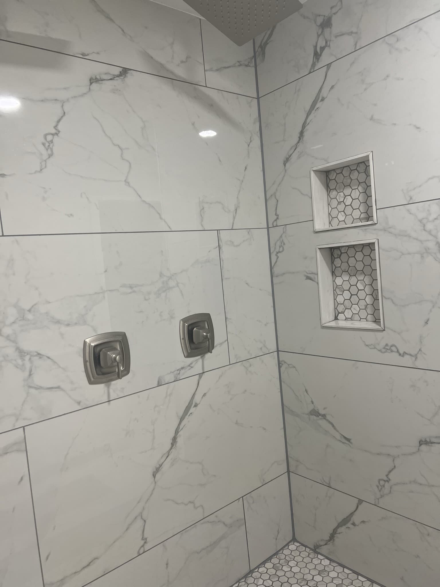 Marble-look porcelain shower wall with brushed nickel controls and stacked niches backed in hexagon mosaic — Karhan Construction, Orlando