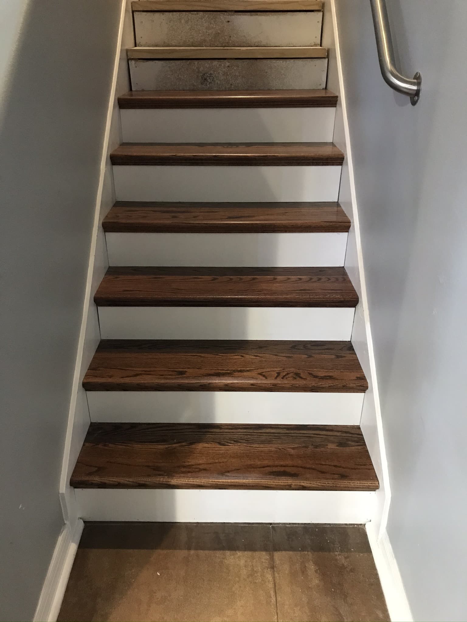 Staircase with new stained red oak treads and white painted risers, top two steps still bare wood, next to a metal handrail — Karhan Construction, Orlando