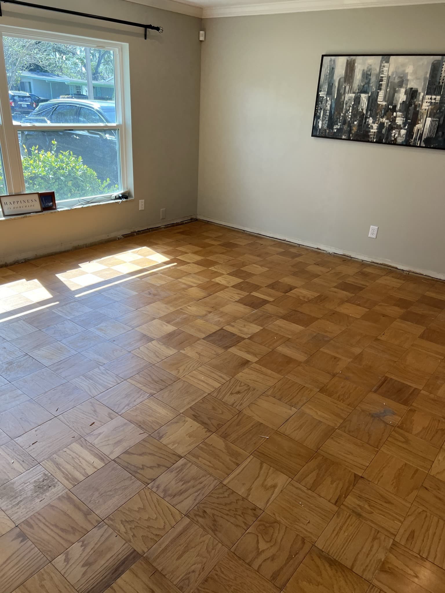 Empty room with original basket-weave parquet wood-block floor, a bright window and framed cityscape art — Karhan Construction, Orlando