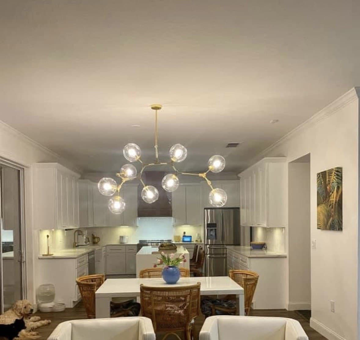 Open great room and white kitchen under a branching glass-globe brass chandelier, dog resting on the wood floor — Karhan Construction, Orlando