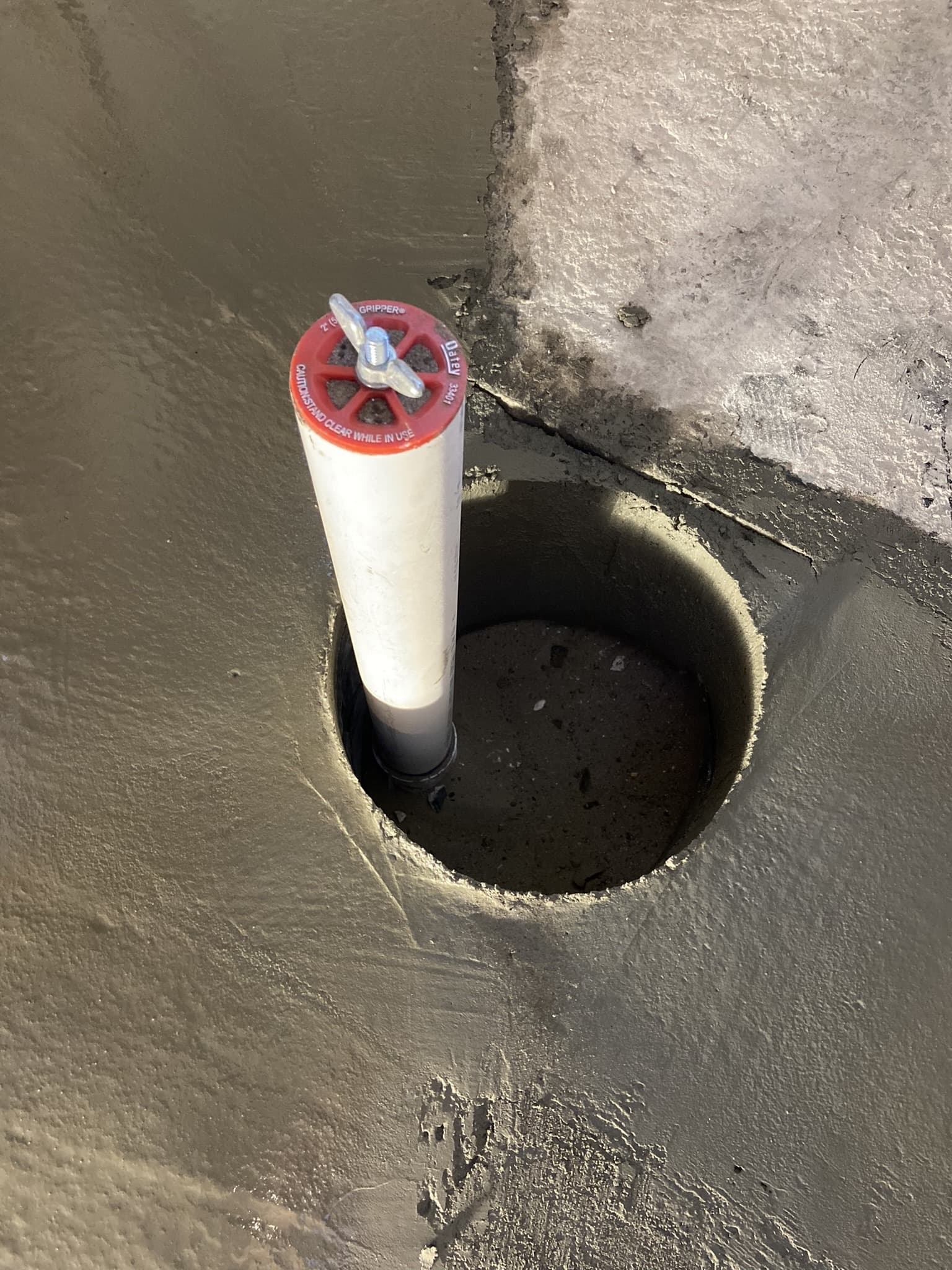 Capped PVC cleanout rising from a cored round hole in a smoothly finished interior concrete floor — Karhan Construction, Orlando