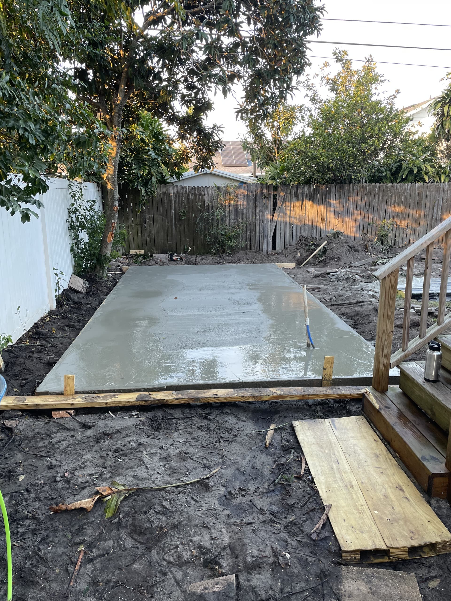 Freshly poured backyard concrete slab with a wet gray finish set inside wood forms beside wooden deck steps — Karhan Construction, Orlando