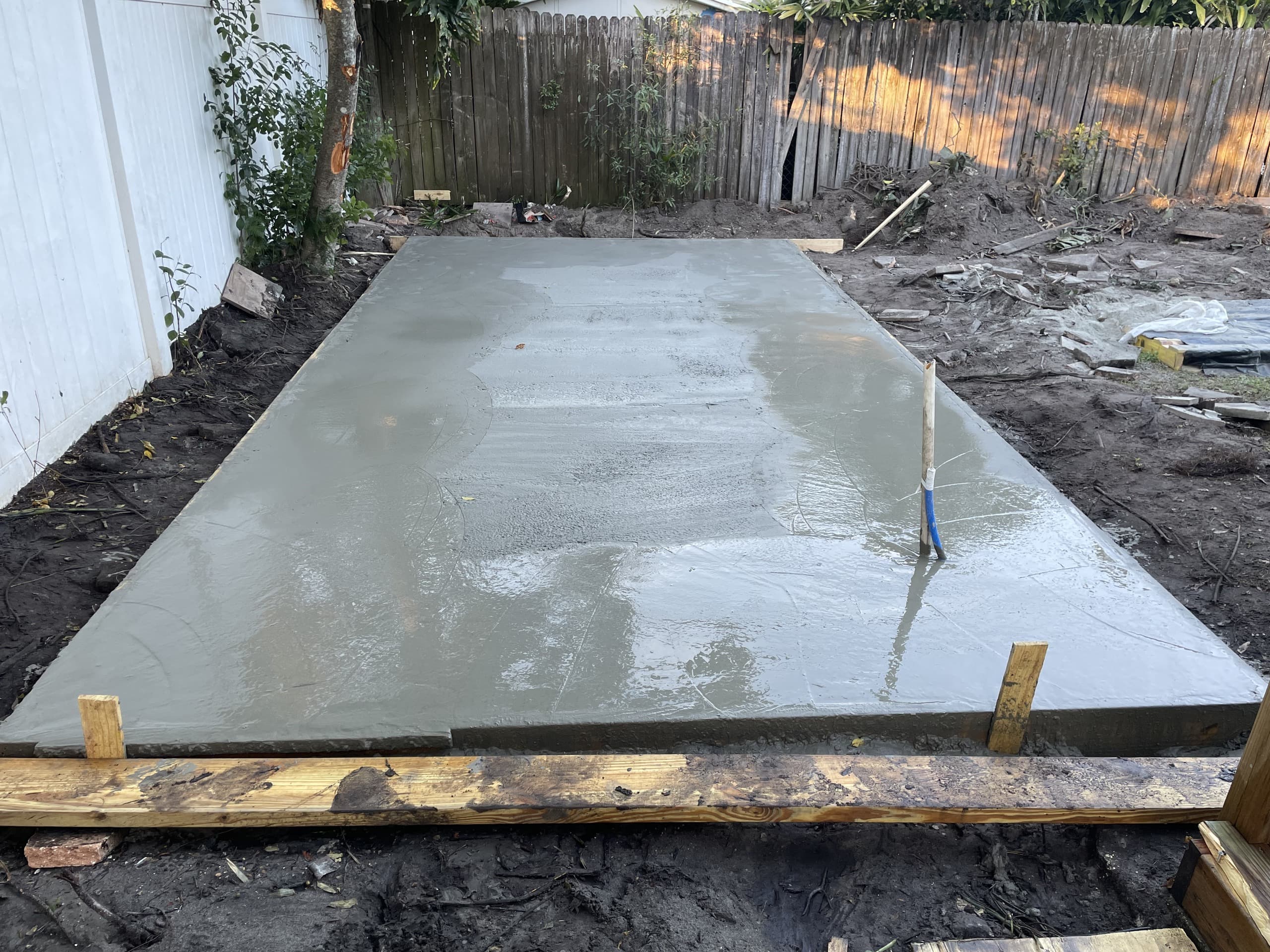 Newly poured concrete slab with a wet troweled surface curing inside timber form boards in a dirt backyard — Karhan Construction, Orlando