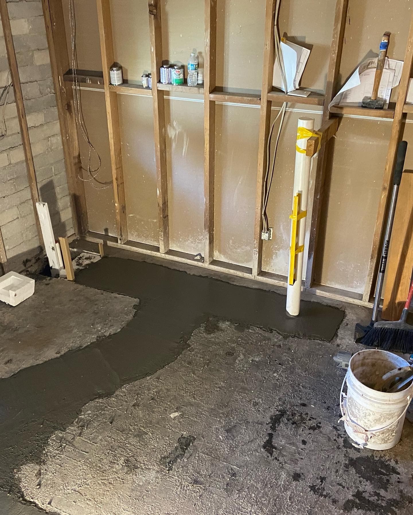 Wet gray concrete floor patch poured along a stud wall base around a white PVC pipe next to the old slab — Karhan Construction, Orlando