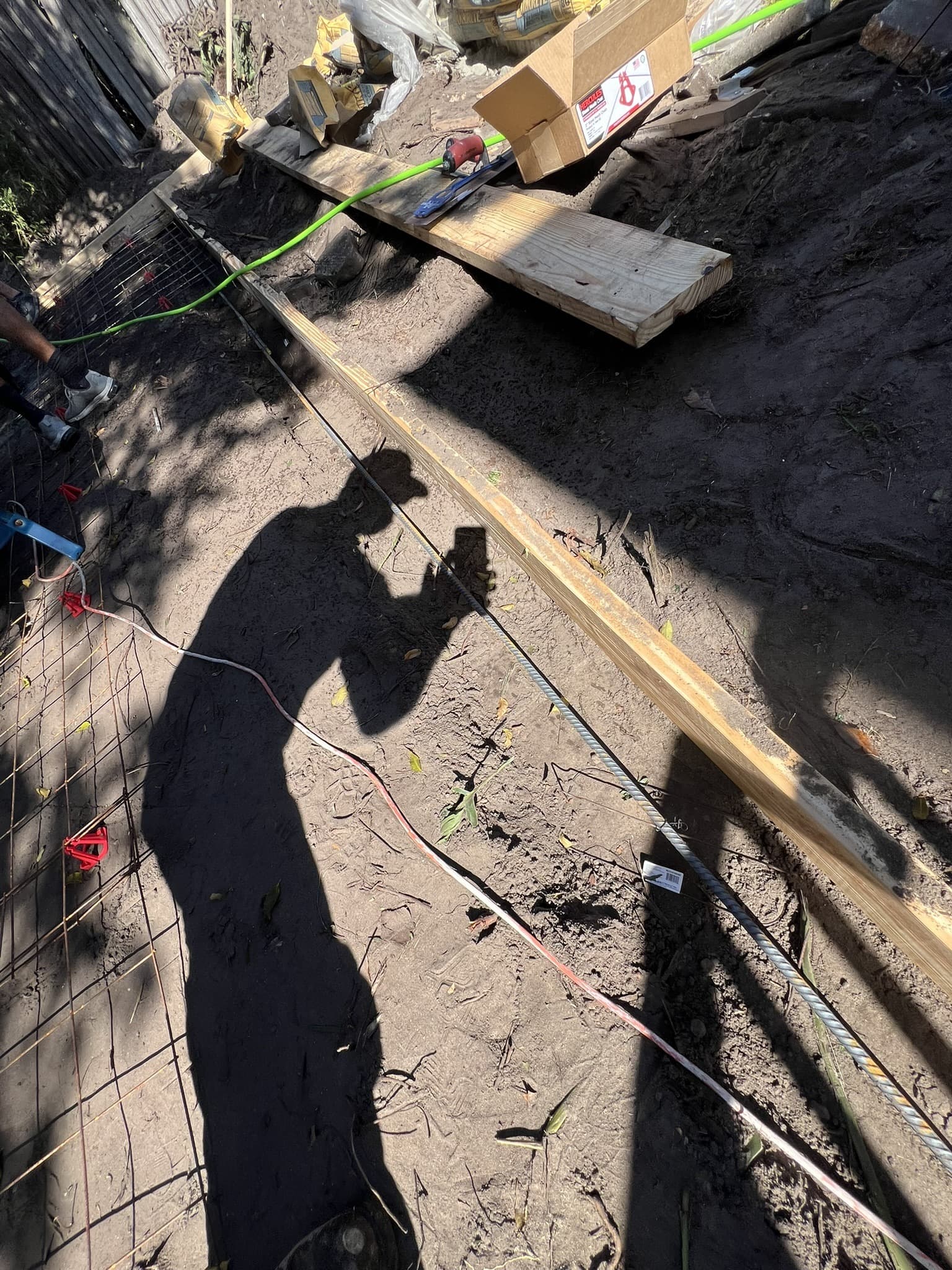 Concrete pour prep with wire mesh, rebar and a screed board over sandy soil, worker shadow cast across it — Karhan Construction, Orlando