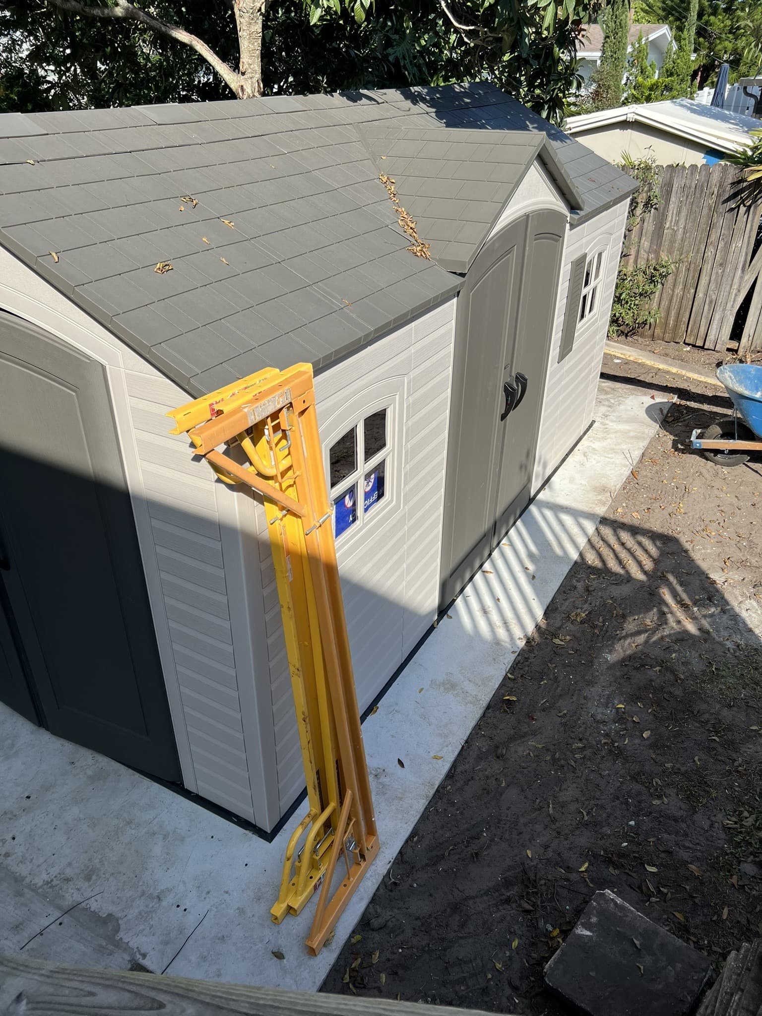 Elevated view of a resin storage shed set on a finished concrete pad with yellow lifting jacks leaning on it — Karhan Construction, Orlando
