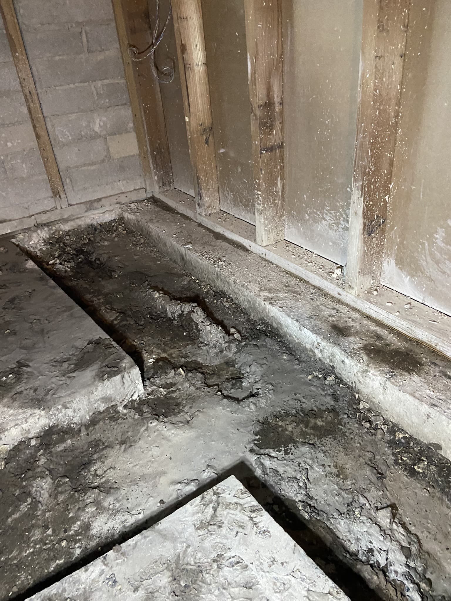 Trench broken out of an interior concrete floor along a stud wall, exposing the gravel base below — Karhan Construction, Orlando