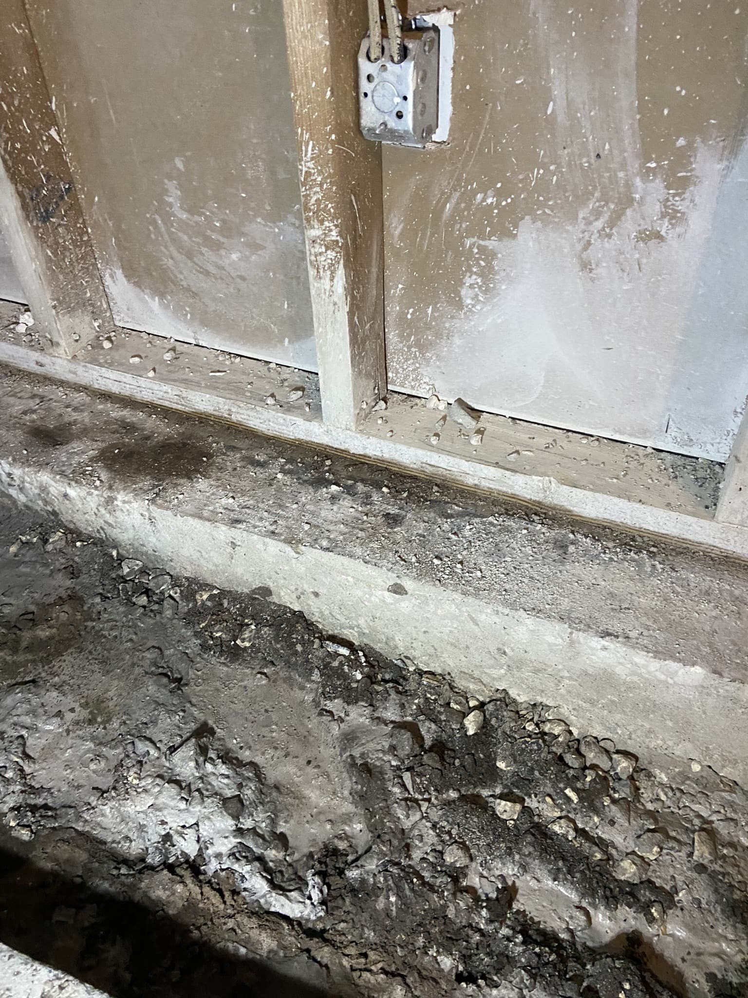 Broken concrete slab edge at a stud wall base with a metal electrical box above, exposed aggregate and dust — Karhan Construction, Orlando