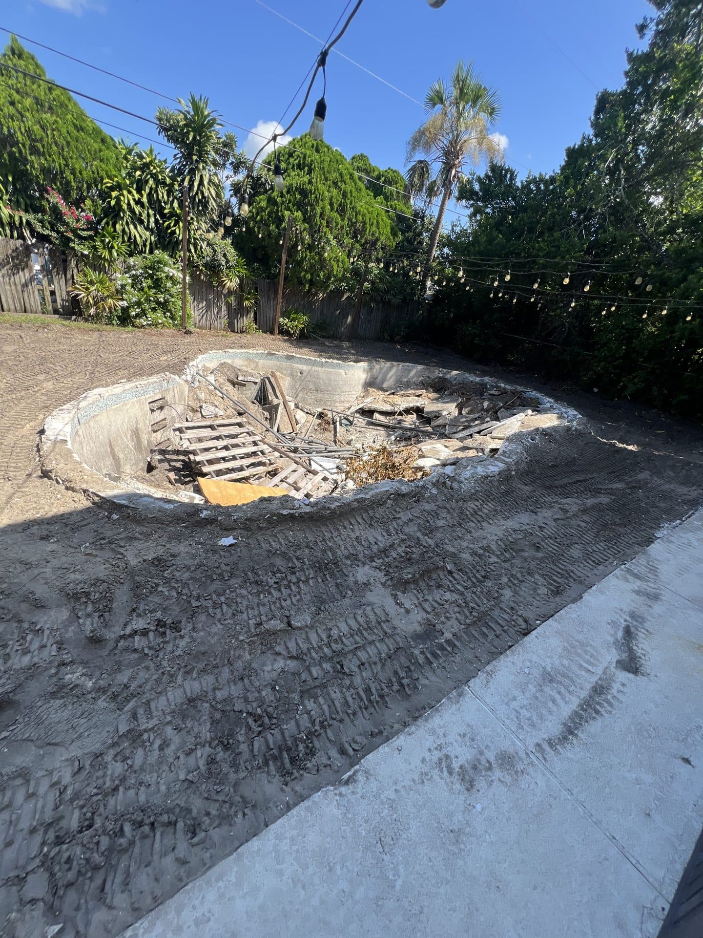Drained concrete pool shell holding wood pallets and rubble, ringed by dirt with tire tracks - Karhan Construction, Orlando