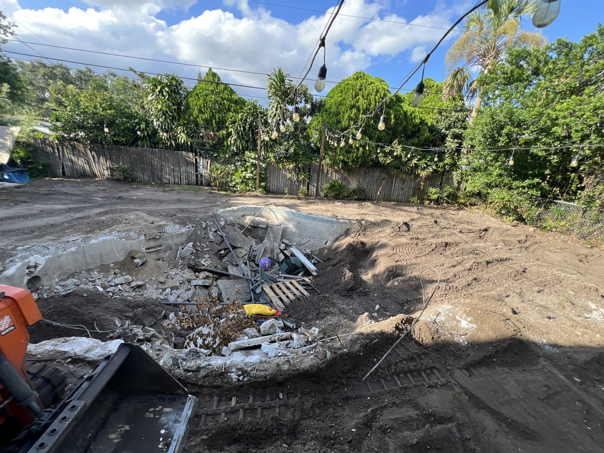 Pool shell partly backfilled with dirt and rubble as an orange rental track loader bucket digs at the edge - Karhan Construction, Orlando