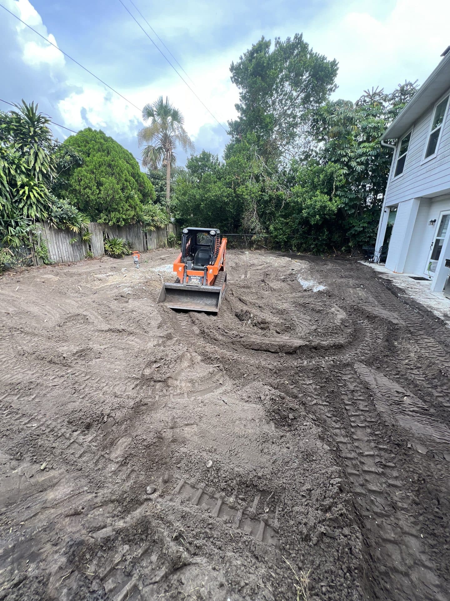 Fully backfilled and graded dirt yard with the pool removed as an orange track loader smooths the soil - Karhan Construction, Orlando