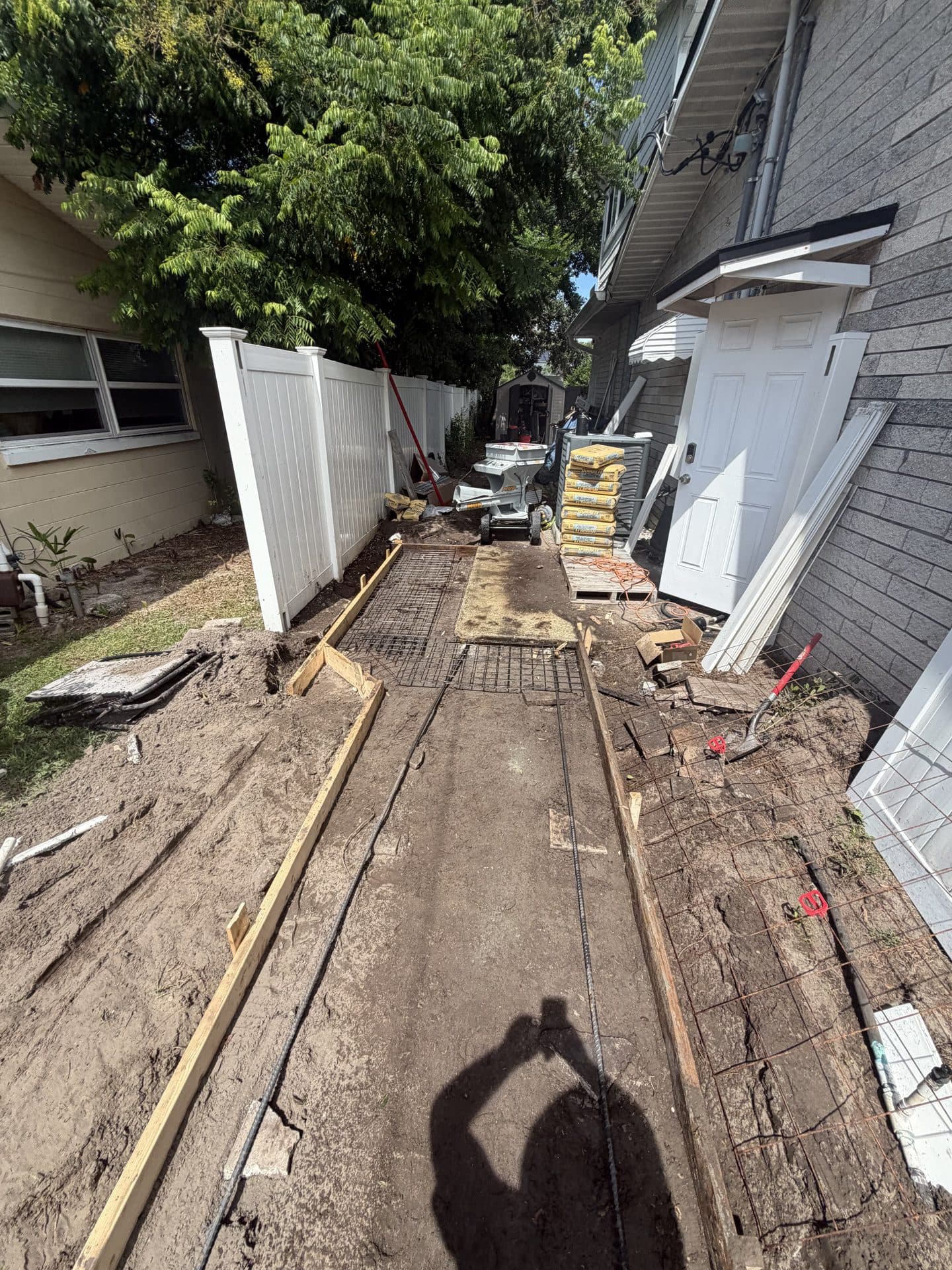 Narrow side-yard walkway framed with wood forms and steel mesh between a white vinyl fence and gray house — Karhan Construction, Orlando