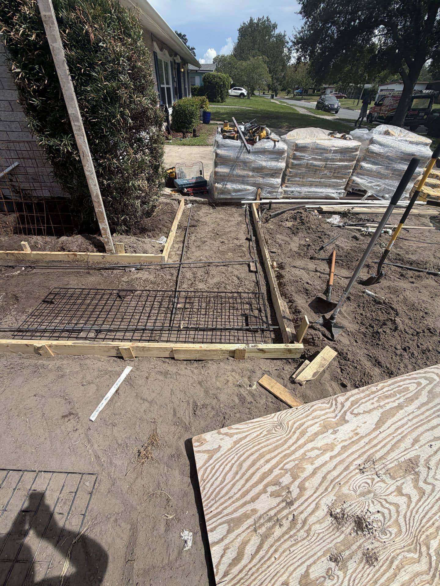 Front-yard walkway forms and wire mesh in soil, pallets of bagged material staged by the street — Karhan Construction, Orlando