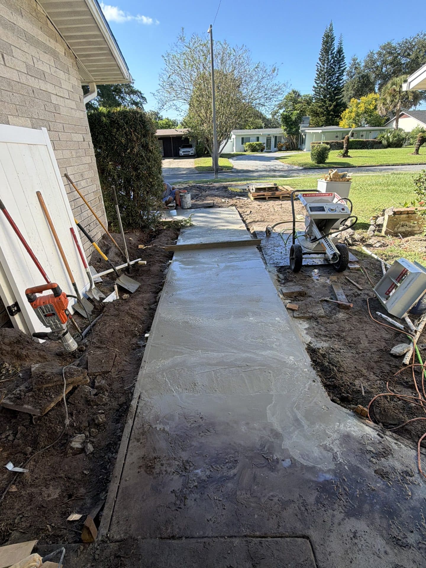 Freshly poured wet concrete sidewalk running to the street, with shovels and a mortar sprayer alongside — Karhan Construction, Orlando