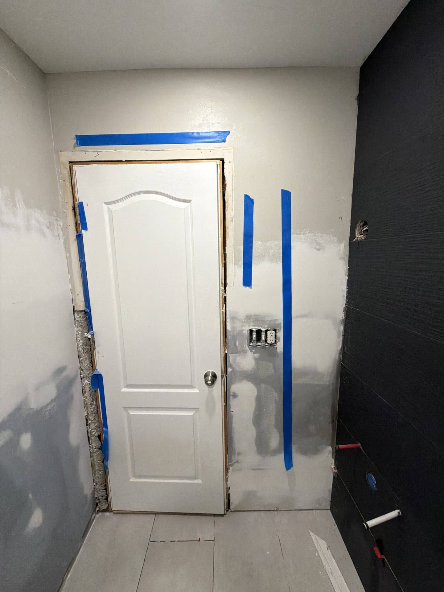 White arched door reset in a skim-coated bathroom wall with blue tape and a dark charcoal accent wall — Karhan Construction, Orlando