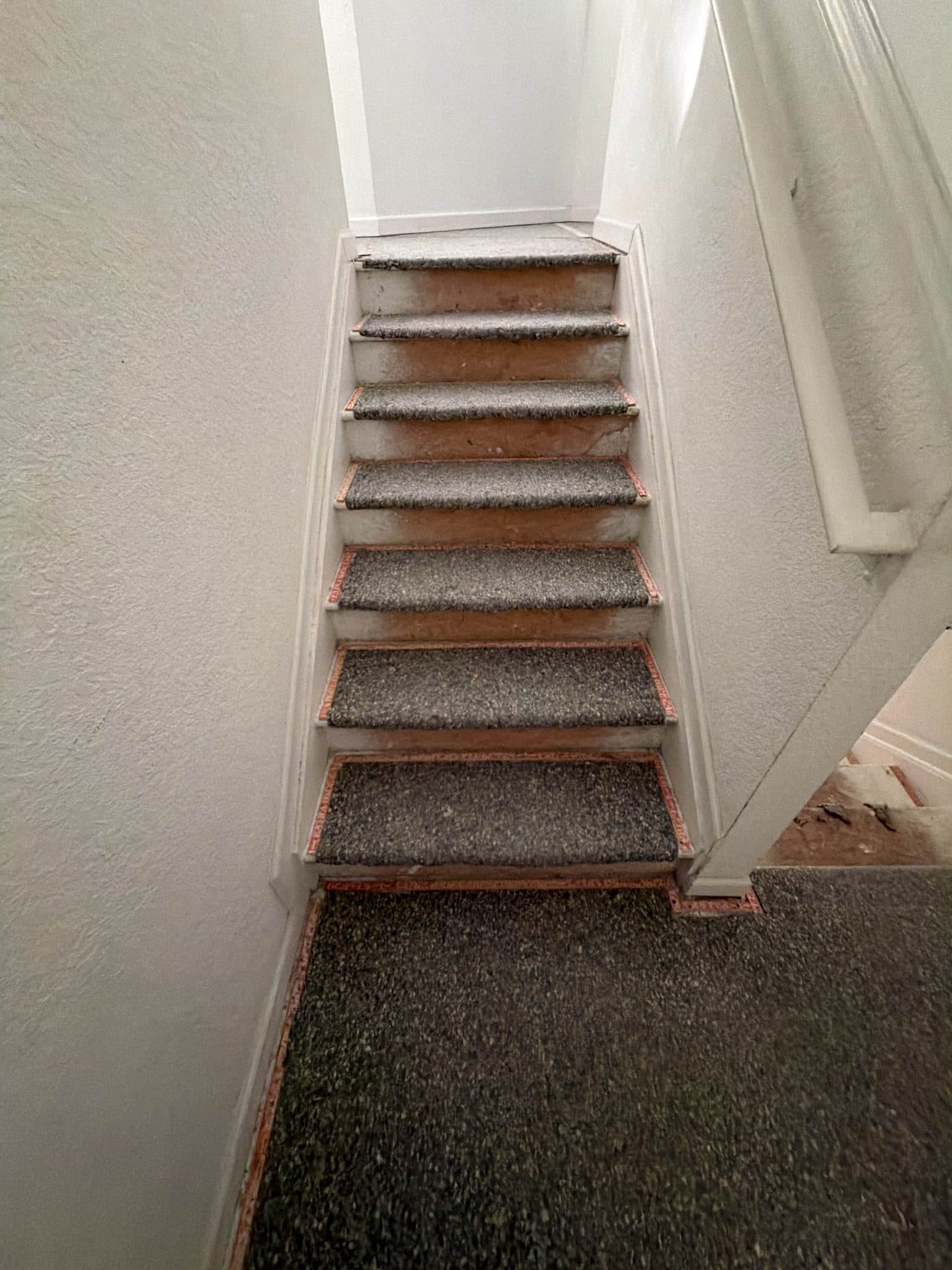 Narrow staircase with worn gray carpet on the treads and exposed particleboard risers before removal — Karhan Construction, Orlando