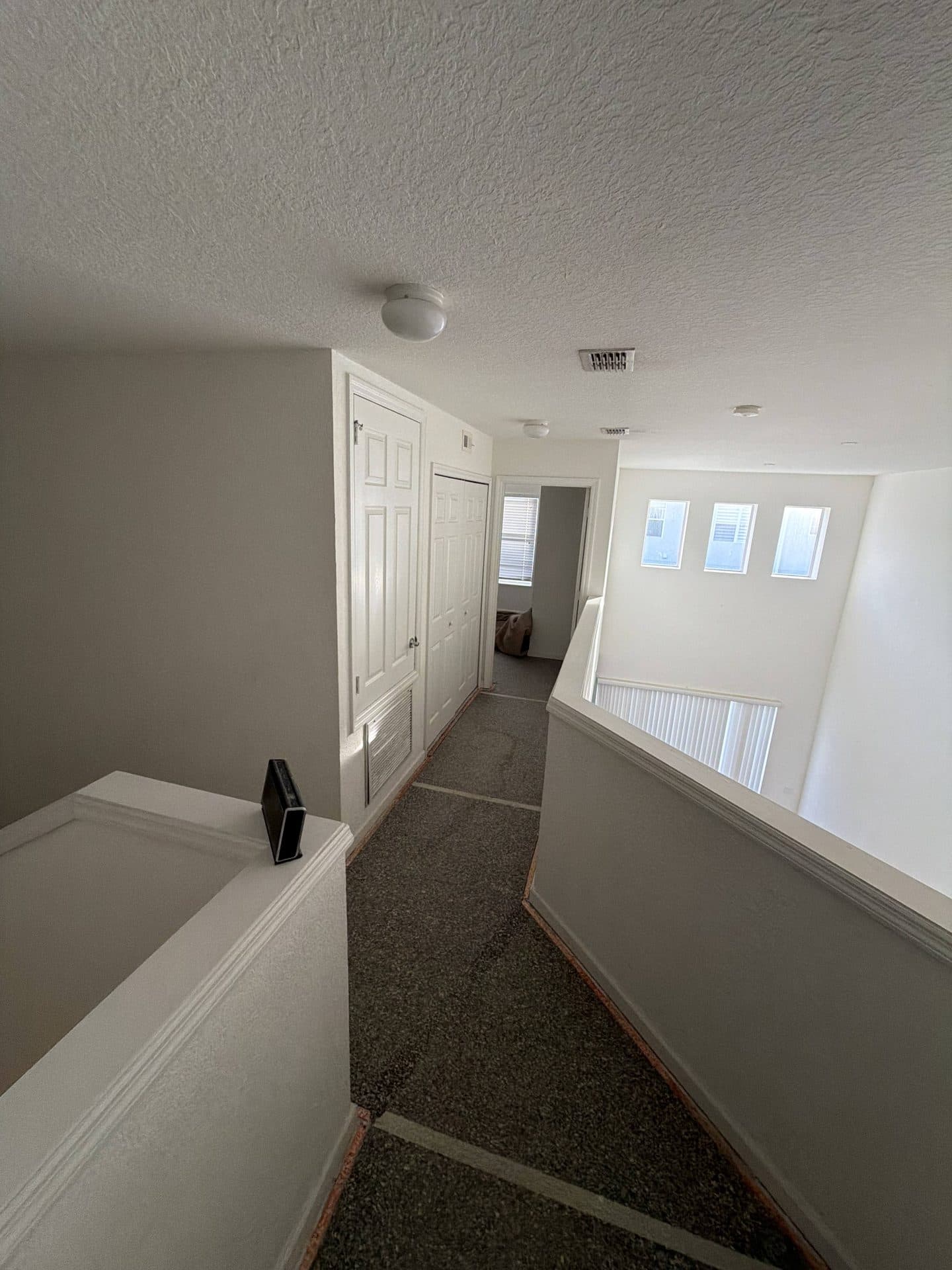 Upstairs carpeted landing with white six-panel doors and an open railing overlooking the lower level below — Karhan Construction, Orlando