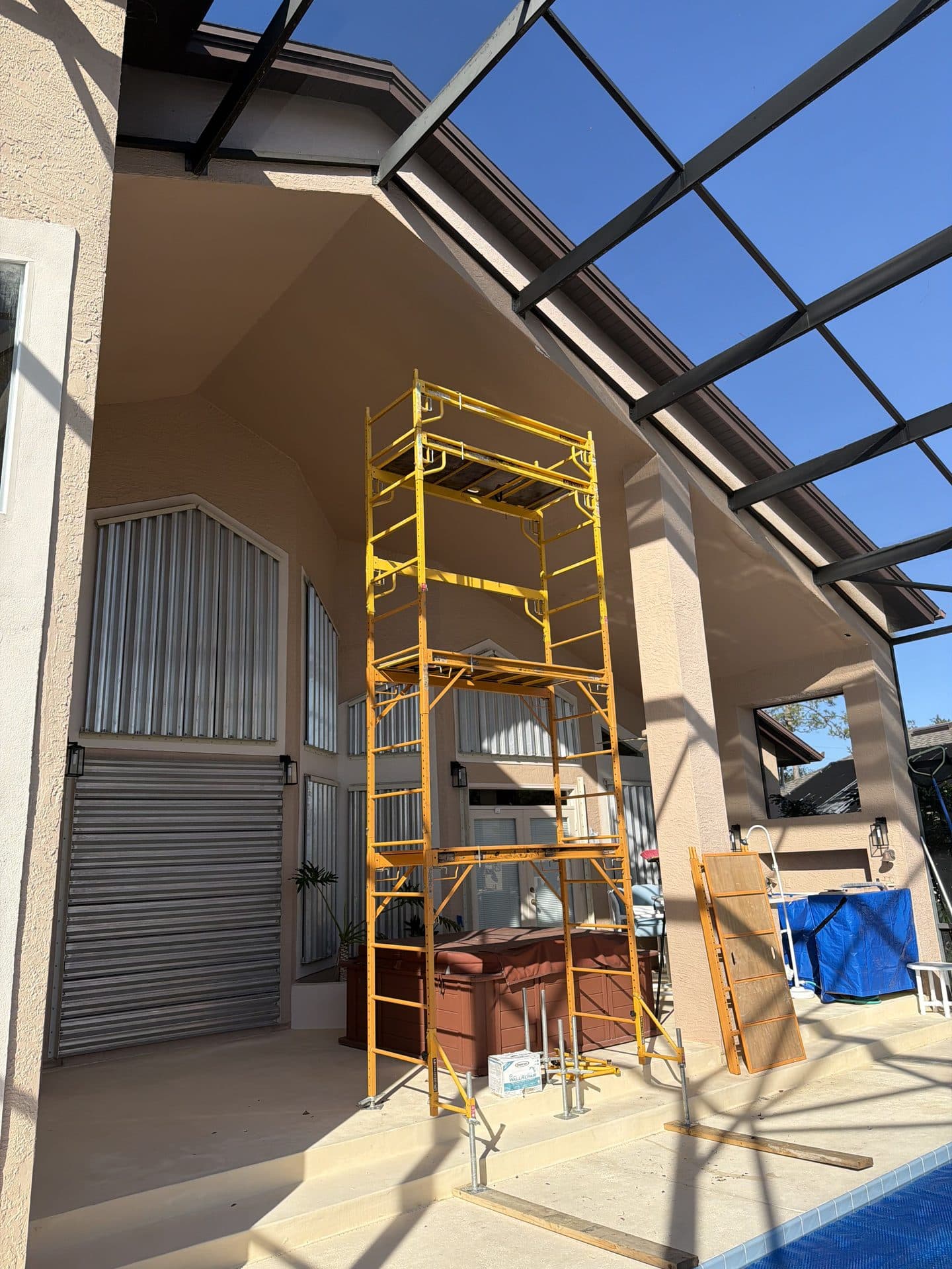 Tall yellow scaffold tower set up on a screened pool lanai to reach the vaulted stucco soffit for repainting — Karhan Construction, Orlando