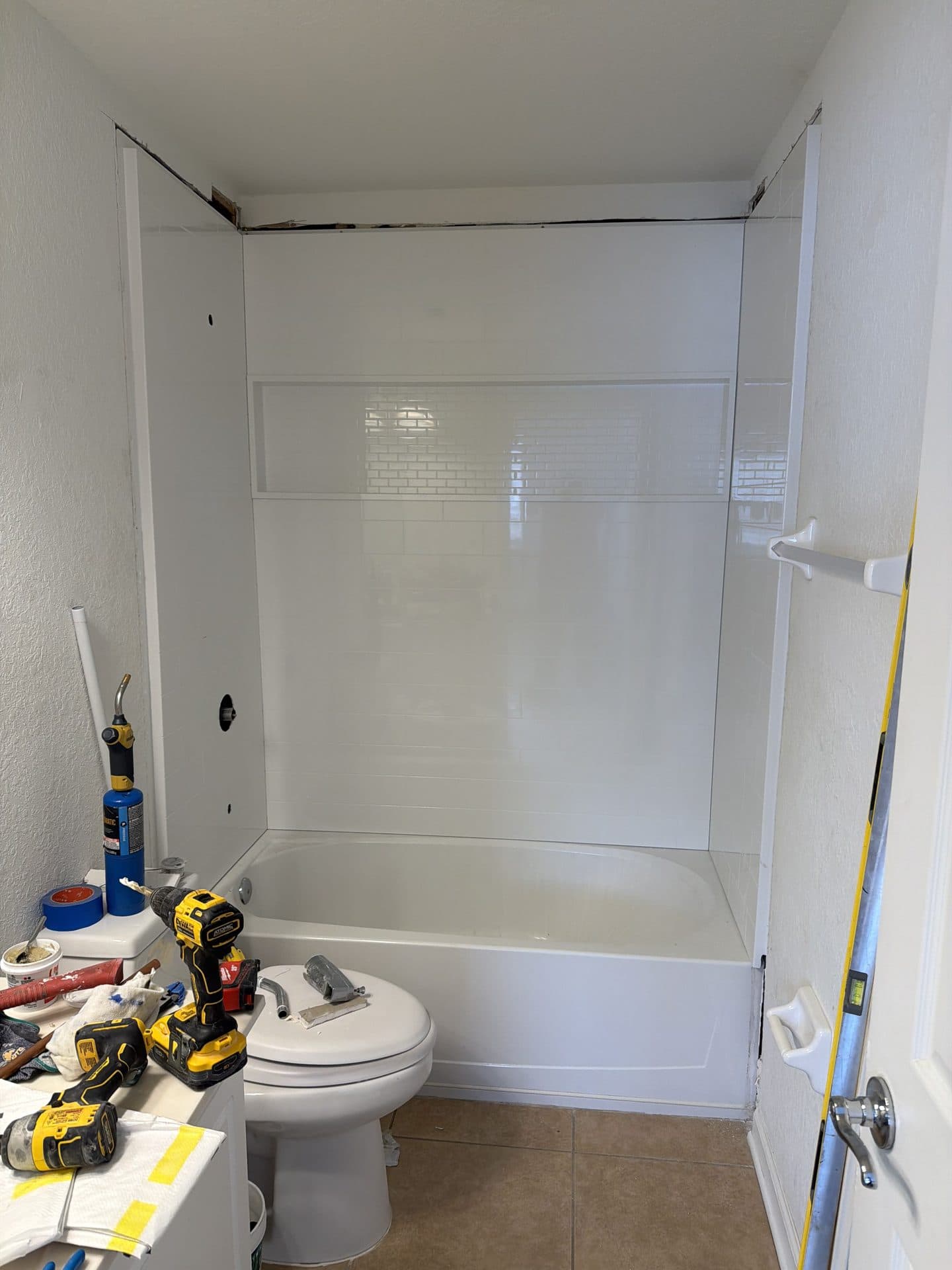 Small bathroom with a white subway-tile tub surround and cordless drills and tools staged on the vanity mid-remodel — Karhan Construction, Orlando