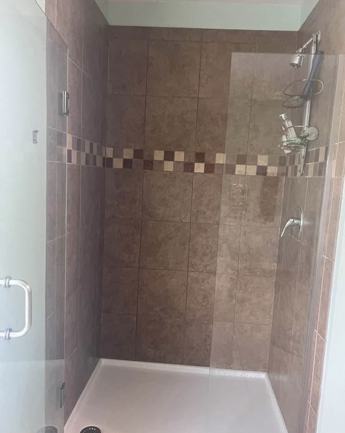 Tiled shower stall in taupe stone-look tile with a brown and cream checkerboard mosaic band and glass door — Karhan Construction, Orlando