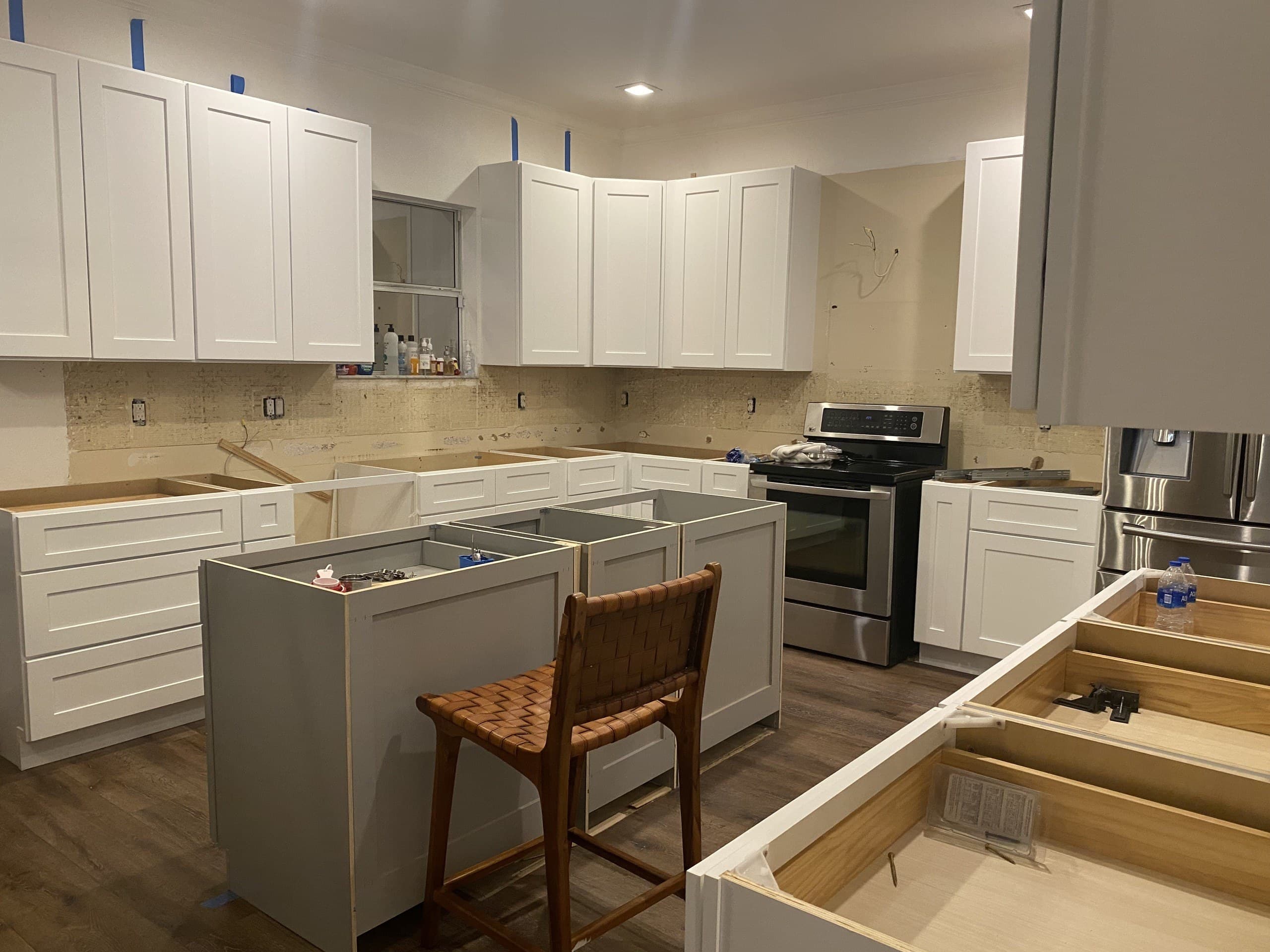 Kitchen cabinet install underway with white perimeter cabinets and gray island boxes, no counters yet — Karhan Construction, Orlando