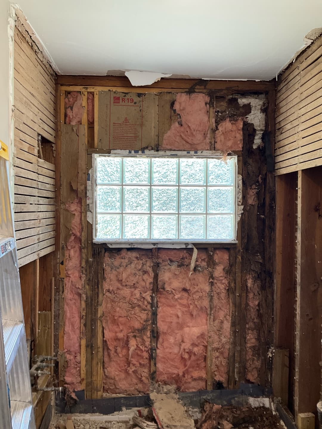 Bathroom demo with walls stripped to studs, exposed pink R-19 insulation and a glass-block window — Karhan Construction, Orlando