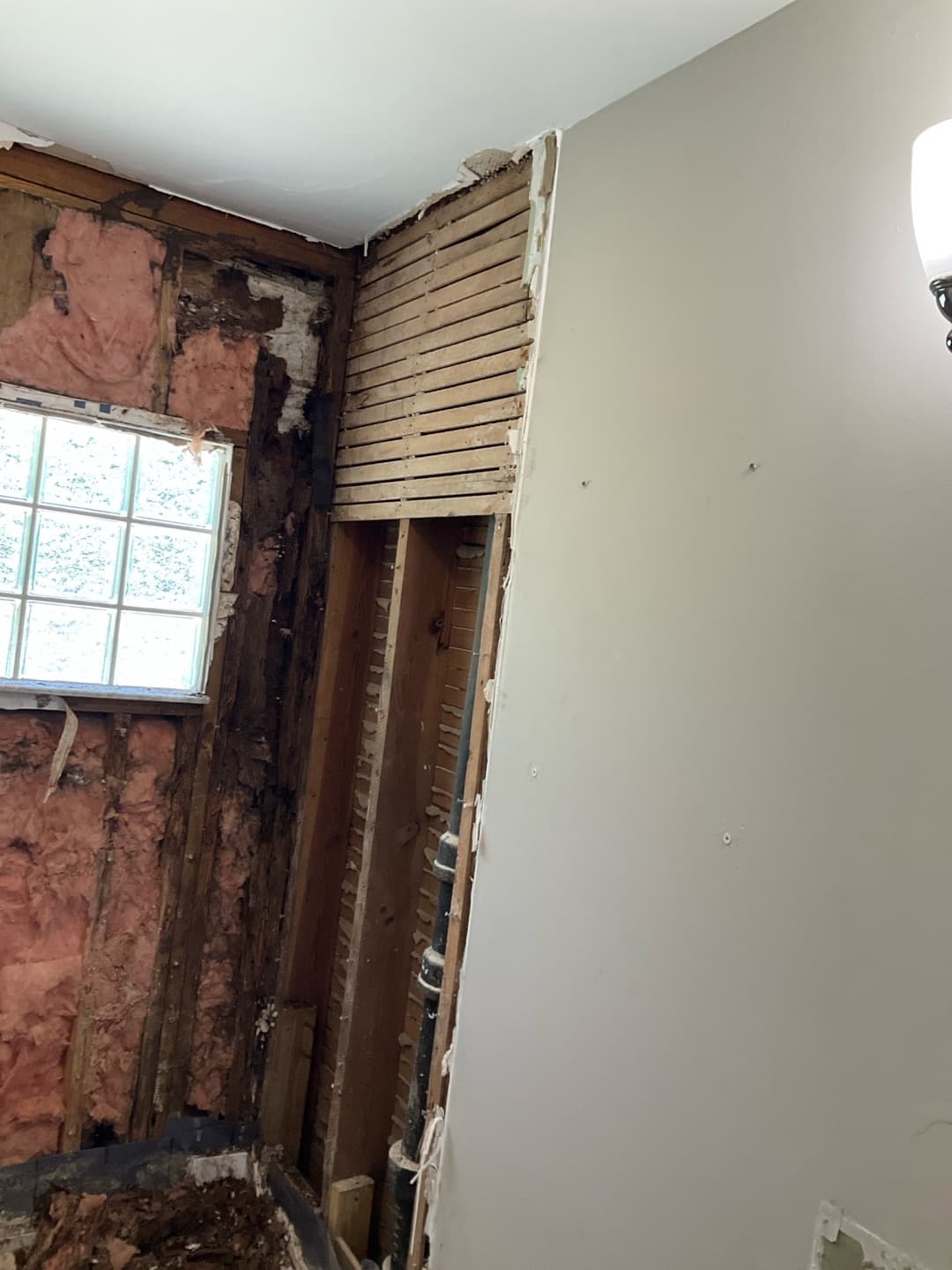 Bathroom tear-out corner: studs and pink insulation beside an intact gray drywall wall with a sconce — Karhan Construction, Orlando