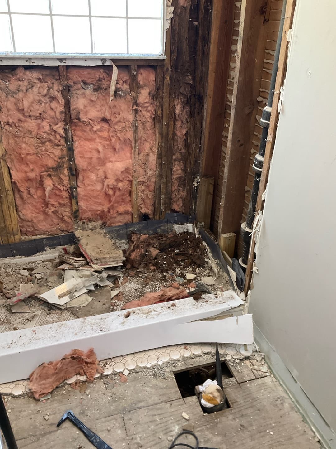 Bathroom demolition with tub torn out, studs and pink insulation exposed and debris piled on the subfloor — Karhan Construction, Orlando