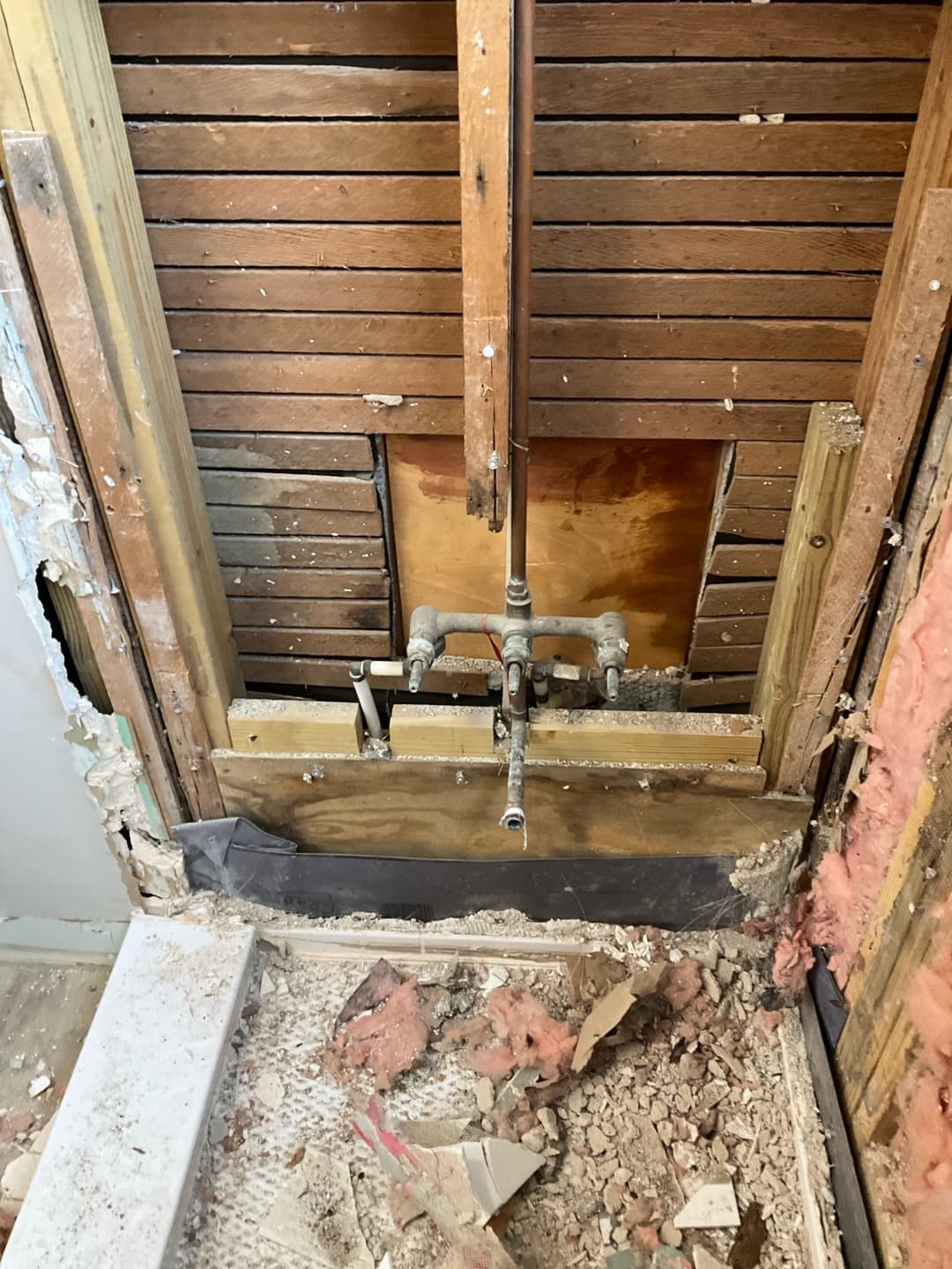 Exposed galvanized shower valve rough-in on a plank wall with demolition debris and black liner below — Karhan Construction, Orlando