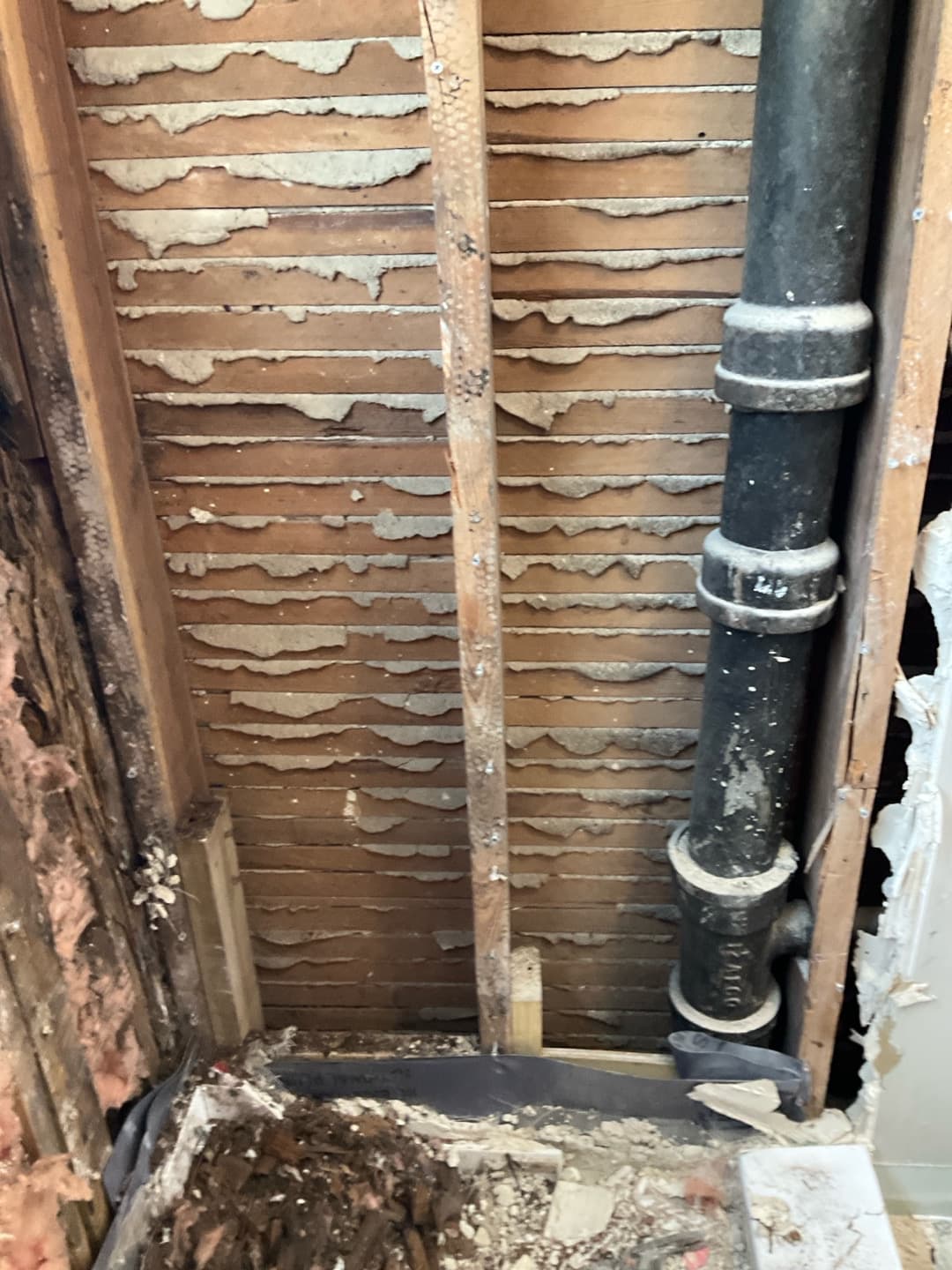 Opened wall showing old wood lath and plaster keys beside a black cast-iron soil stack pipe — Karhan Construction, Orlando