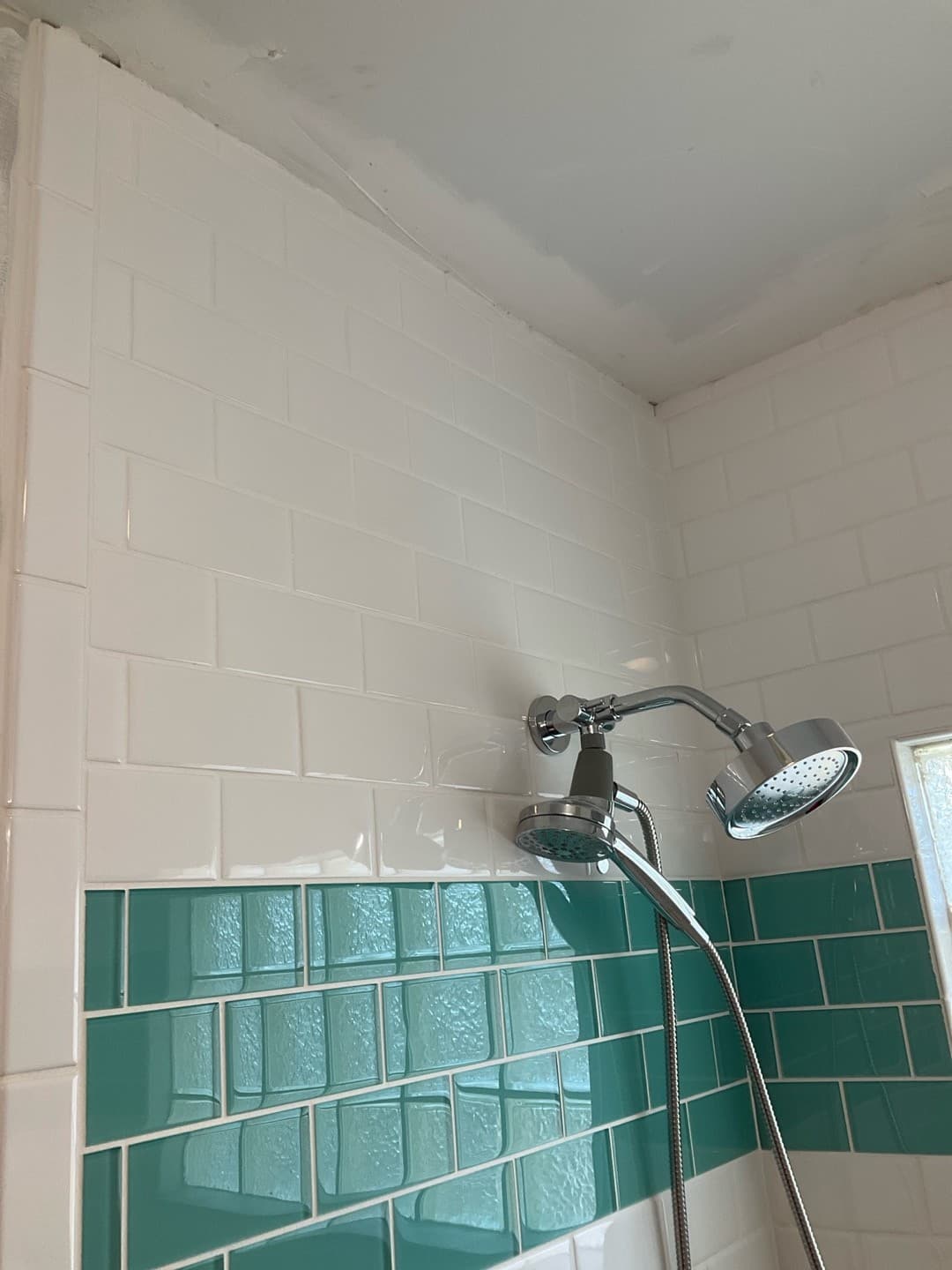 AFTER — shower head and handheld detail against crisp subway tile and the teal accent (real Karhan project)