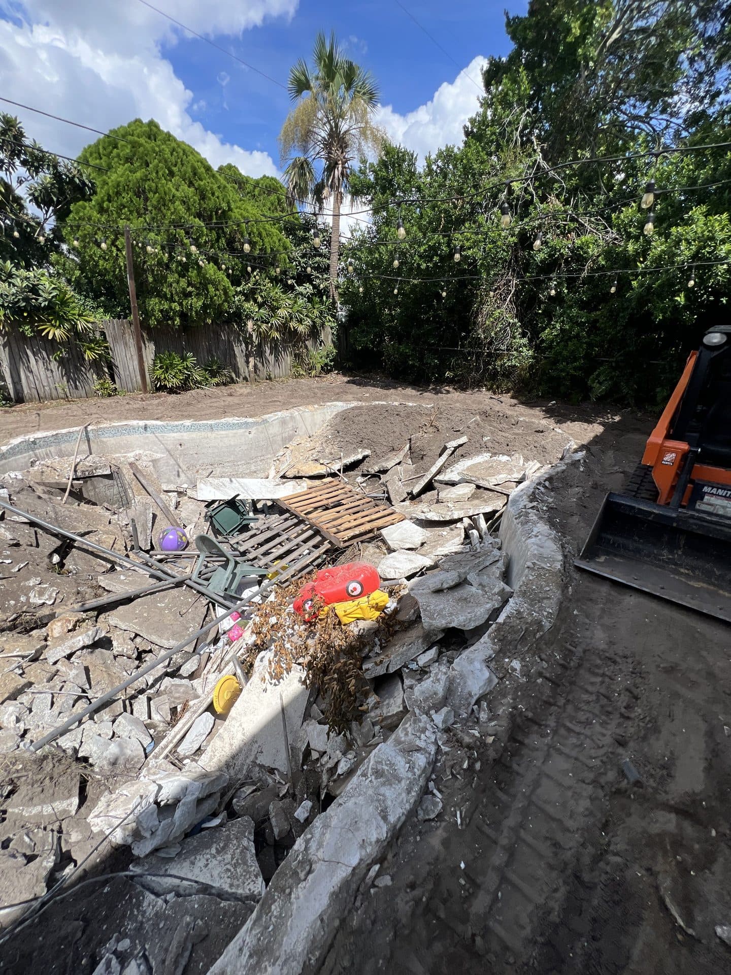 DURING — broken pool coping collapsing into the debris pile beside the track loader bucket (real Karhan project)