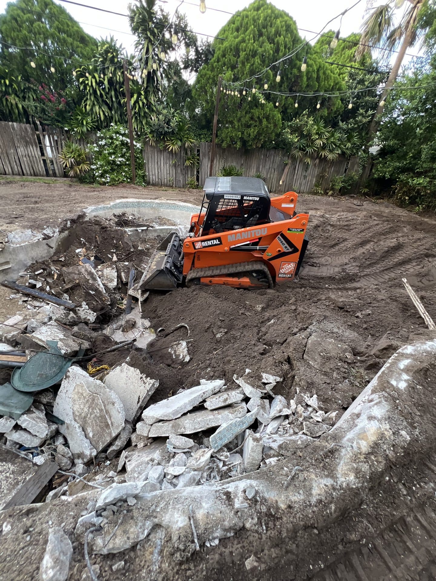 DURING — track loader pushing dirt into the pool pit above broken white concrete and blue tile (real Karhan project)