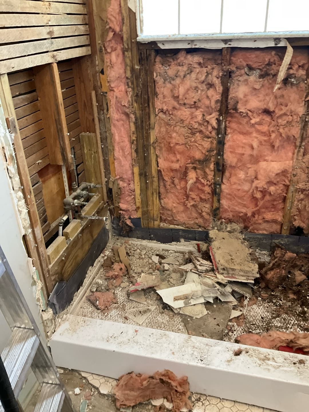 Wide demo view from the doorway — shower stripped to studs, exposed plumbing, debris in the old pan (real Karhan project)