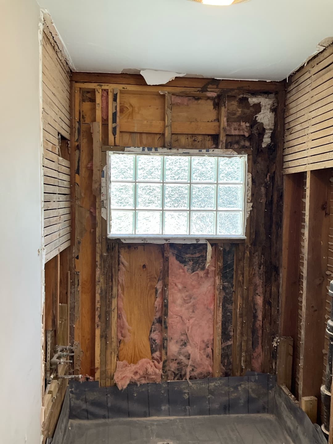 The glass-block window wall opened to the studs during demo, rot visible in the framing (real Karhan project)