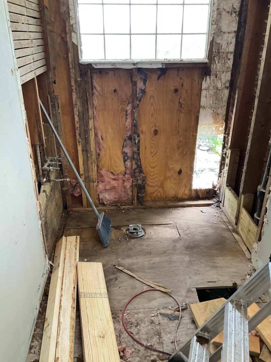 Shower bay stripped to studs, sistered repair on a rotted stud, stubbed copper plumbing, and a floor drain flange, with lumber staged for the rebuild (real Karhan project)